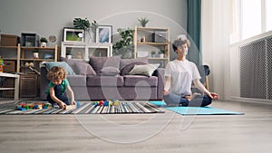 Mom relaxing in lotus position while calm child playing with toys wooden blocks