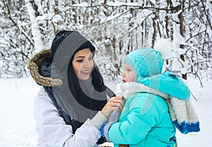 Mom remedies a clothing to the little son in a winter park