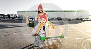 Mom rolls a boy and a girl in the grocery cart of the children near the supermarket