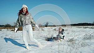 Mom rolls her son on a sled, happy family in the winter, fun entertainment for the mother and child, sledding in the