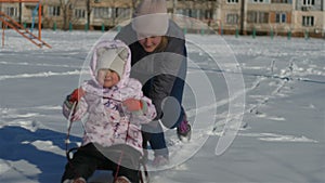 Mom rolls a little daughter in the snow in the sled