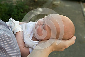 Mom`s hands are holding the baby carefully. A serious and beautiful newborn baby is sleeping. The concept of maternal tenderness