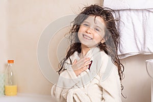 Mom`s hands are washed kid hair with shampoo in the bathroom. Portrait of a beautiful brunette little girl with wet hair, blue eye