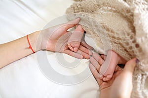 Mom`s holding in hands tiny feet of newborn baby, covered knitte