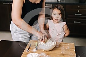 Mom`s kneading the dough for her little girl who makes cheesecakes.