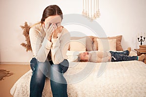 Mom& x27;s tired. A two-year-old girl lying on the bed hysterically screaming crying. The woman is unhappy, covers her face