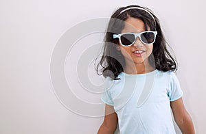 Mom says Im the coolest kid on the block. Shot of an adorable little girl wearing sunglasses while standing against a