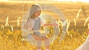 Mom shakes her healthy daughter on a swing under a tree in the sun. happy family. healthy child flies on a swing in the