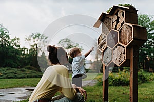 Mom showing her playful son an insect hotel in public park.