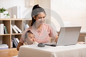 Mom is showing something on the screen for an infant. The baby boy has an attention with laptop. Smiling mother is make a kid feel