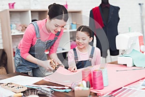 Mom shows the girl how to cut fabric.