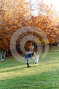 Mom shows a little girl a bouquet of yellow leaves leaning towards her standing on a green lawn