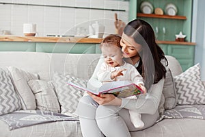 Mom sits on a sofa with a child, reads a book and looks at bright pictures