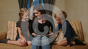 Mom sitting on the couch with his daughter and young son, reading them a story while sitting on the couch in their