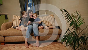 Mom sitting on the couch with his daughter and young son, reading them a story while sitting on the couch in their