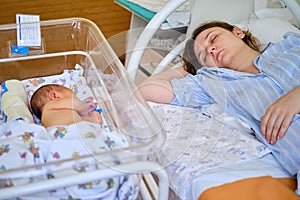 Mom is sleeping in the ward with a newborn baby, a maternity hospital bracelet on her arm. A newly born child in a clinic crib