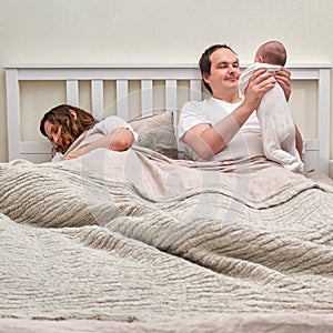 Mom sleeps while father takes care of baby boy, parents and infant child on the home bed. Problems of a man and a woman with a