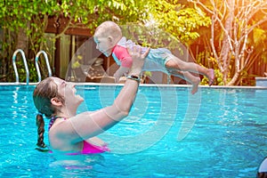 Mom with a small child of eight months having fun and swimming in the pool. Summer vacation at sea. Woman holding a child over her