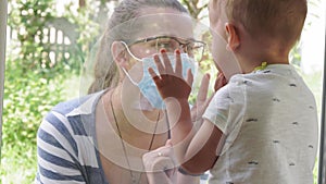 Mom with a small child in a medical mask look out the window during quarantine by reason of coronavirus, covid-19 virus