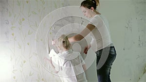 A mom and a small daughter removing old wallpaper.