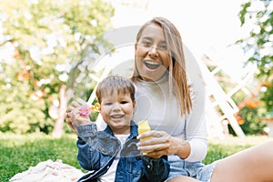 Mom and son are blowing soap bubbles in a summer park