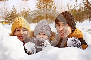 Mom, son and dad are hiding behind snow wall and throwing snowballs.