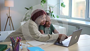 Mom, son doing homework and using laptop while sitting at table in apartment room spbd.