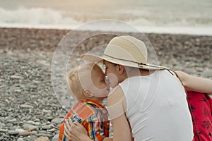 Mom and son embrace on a pebble beach. Sunset time. Back view