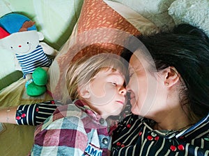 Mom and son lie on the bed, hugging each other and kissing. Mother with her son are having fun lying on top of each