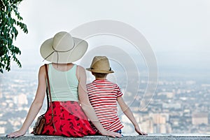 Mom and son and look at the city from a height. Rear view, evening time