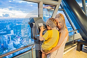 Mom and son are looking at Kuala lumpur cityscape. Use binoculars. Panoramic view of Kuala Lumpur city skyline evening