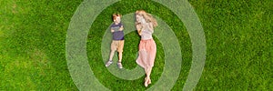 Mom and son are lying on the grass in the park. Mom looks at the phone, son looks at the tablet. Photos from the drone