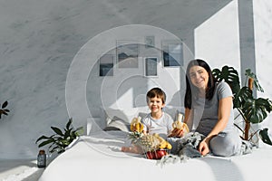 Mom with son in pajamas eating fruit on bed. portrait happy, smiling, joyful family, mothen and son having breakfast in bed,