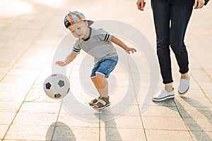 Mom and son play football together outdoors in the park, Little boy kicks a soccer ball, child learns to play football