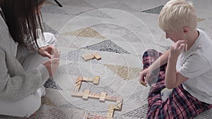 Mom and son play at home in wooden dominoes.