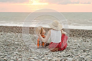 Mom and son play on the pebble beach. Sunset time. Back view