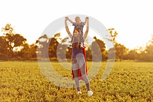 Mom and son play superheroes during the day outdoors. Mom holds the child on her shoulders, play and have fun together