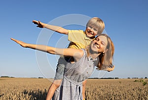 mom and son play together in nature. woman holds child from above on back, cheerfully spreading arms and laughing