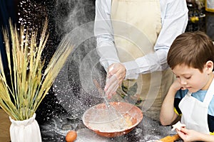 Mom and son play with wheat flour before baking cookies at home in the kitchen. On the table is a pitcher of ears of wheat, a bowl