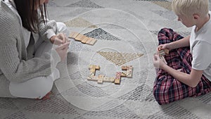 Mom and son play in wooden dominoes at home on the floor in winter