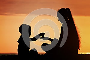 Mom and son playing on the beach with stones. Sunset time, silho