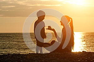 Mom and son playing on the beach with stones. Sunset time, silhouettes