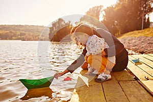 Mom and son playing with paper boats by the lake