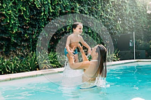 Mom an son playing into the water in a swimming pool.