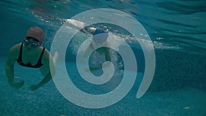 Mom and son in the pool are swimming a race under water