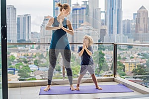 Mom and son are practicing yoga on the balcony in the background of a big city. Sports mom with kid doing morning work