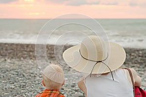 Mom and son rest on the pebble beach. Sunset time. Back view