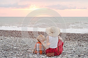 Mom and son rest on the pebble beach. Sunset time. Back view