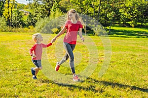 Mom and son run on the green grass. Happy family in the park
