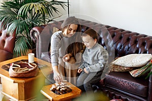 Mom and son sit on sofa living room  building tower from wooden blocks  taking tiles in turn from underneath untill it falls.